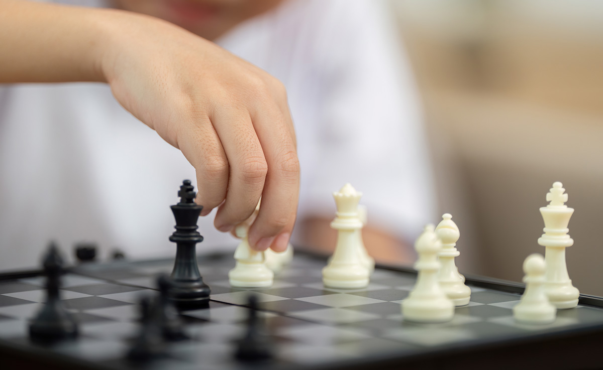 A close-up of a child's hand moving a white chess piece on a chessboard during a game.