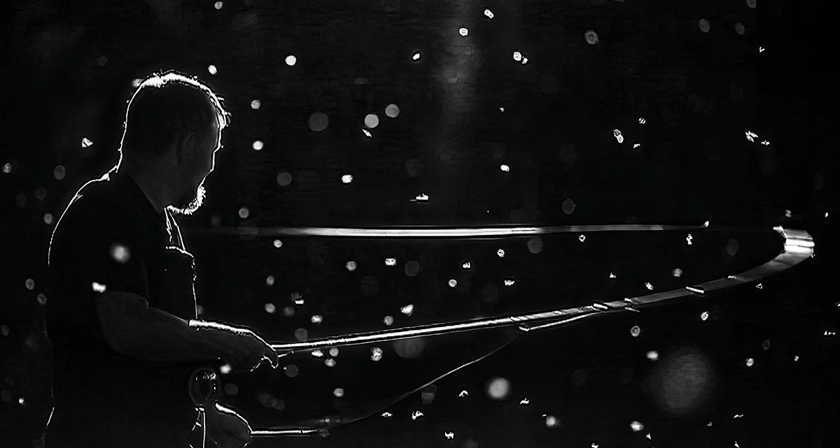 Dramatic black and white high-contrast photo of a person fly fishing. The fishing line arcs across a dark background filled with sparkling bokeh lights.