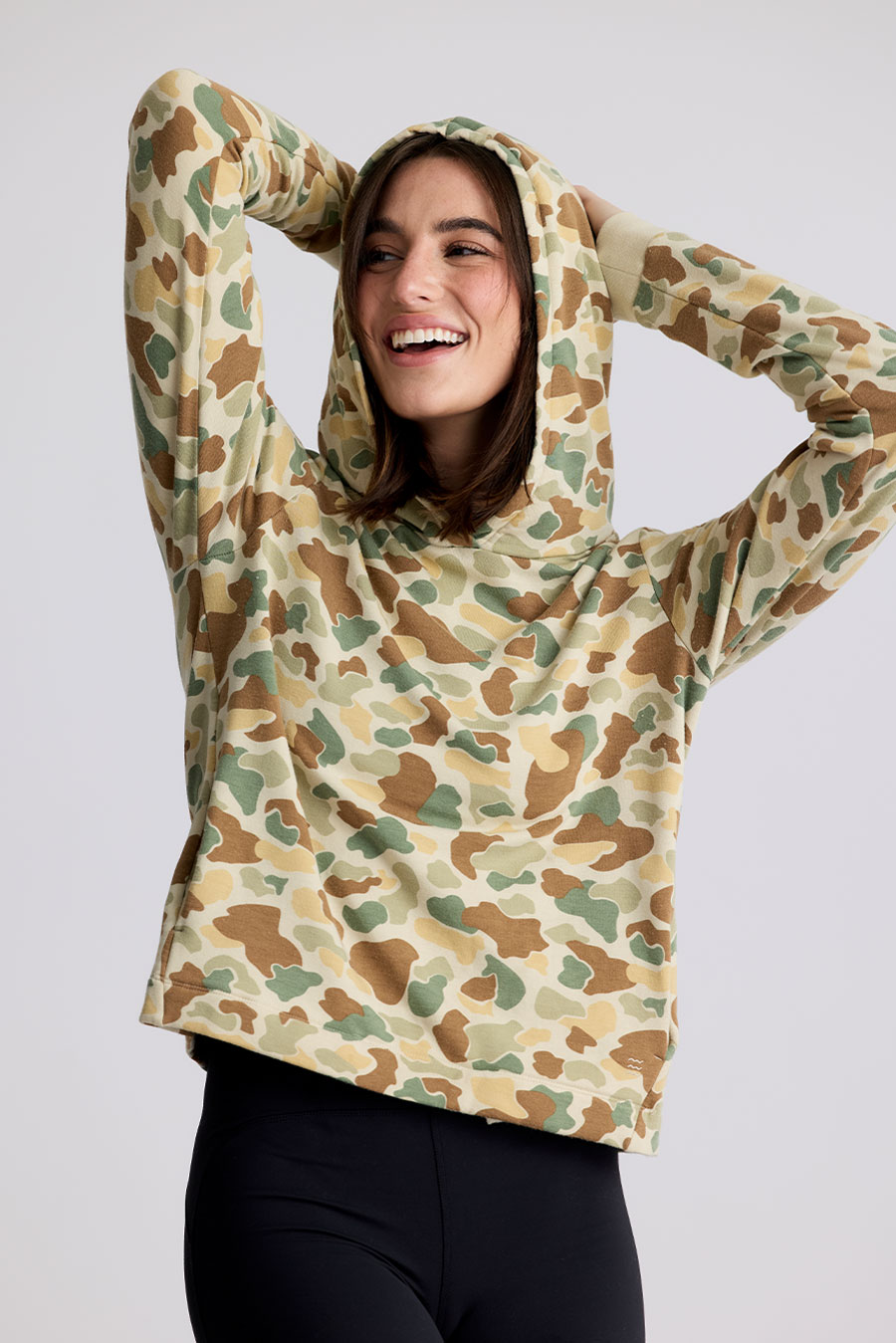 a female model wears a Fly Apparel Bamboo Lightweight Fleece Hoodie with a playful camo pattern 