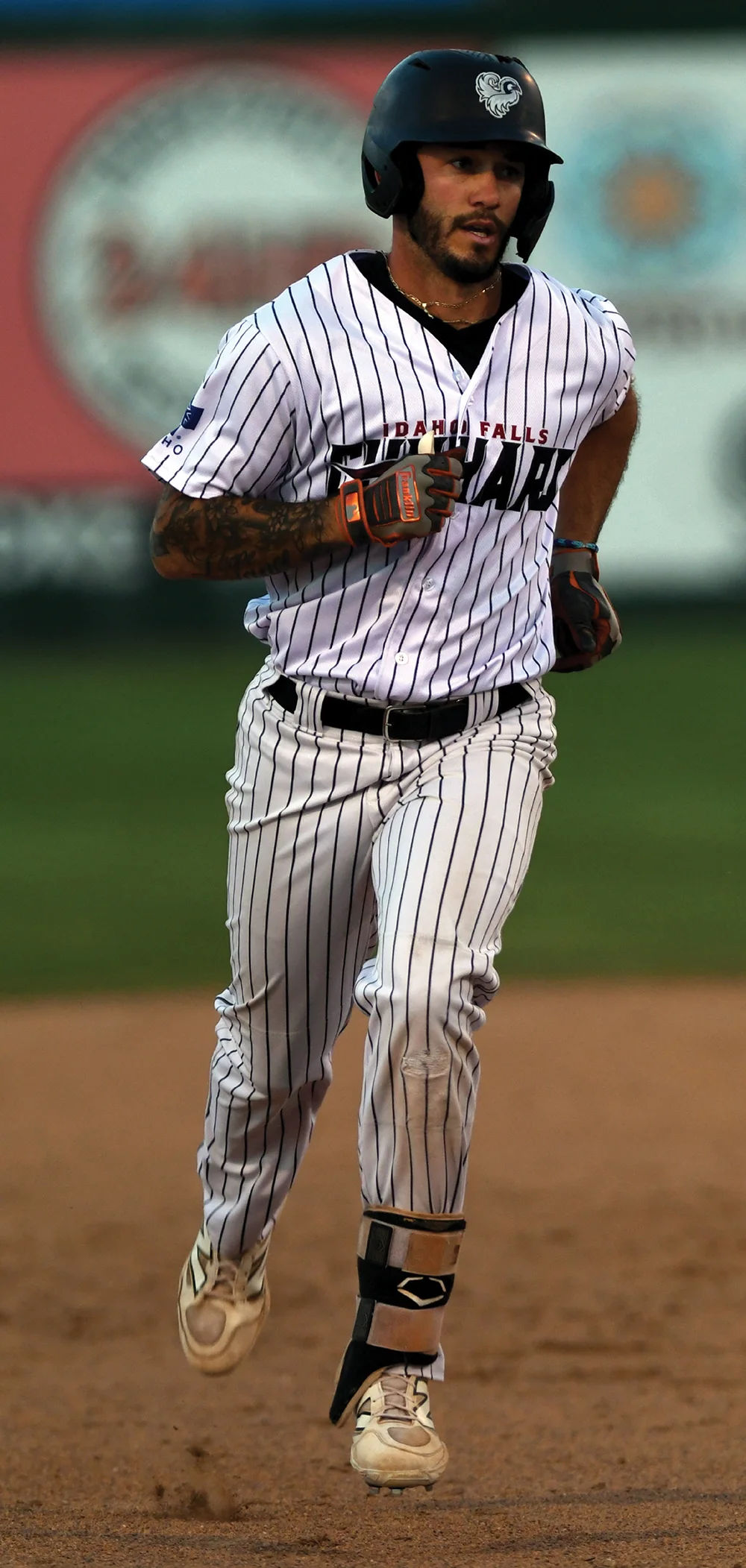 A baseball player in a pinstriped uniform and helmet running across the field, showcasing tattoos on his arm.