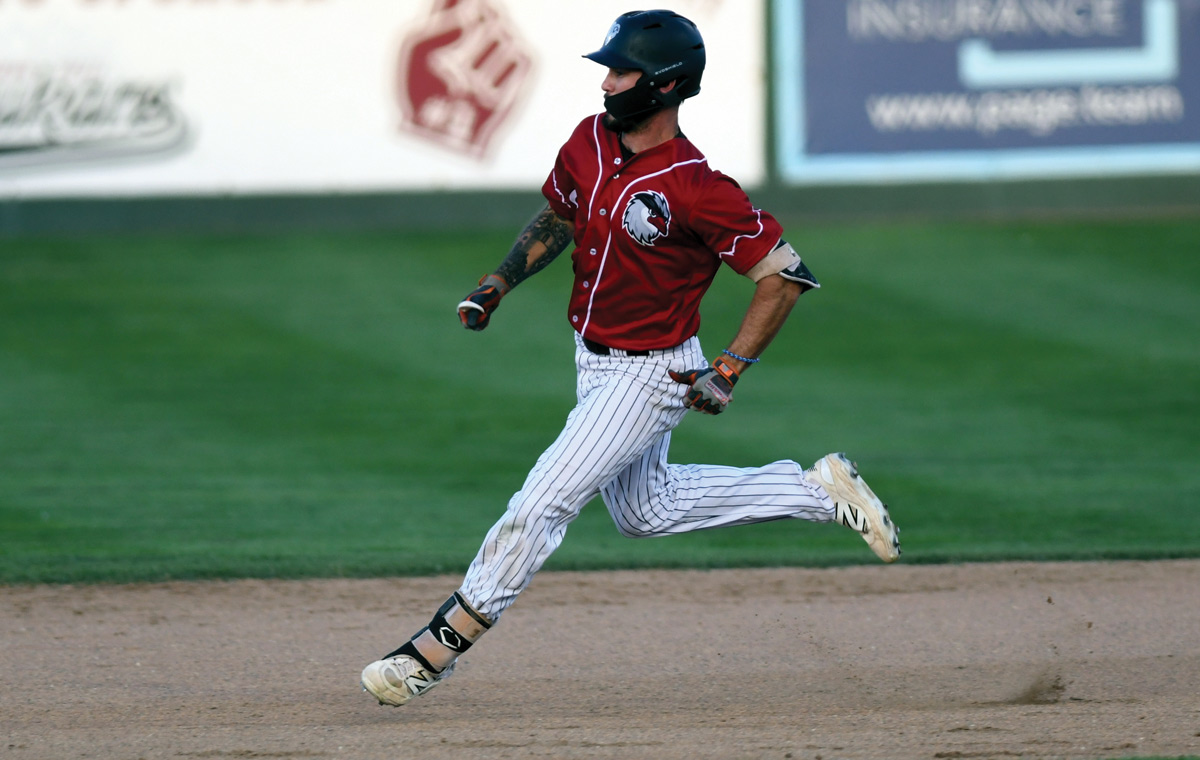 Side view of a baseball player wearing a red jersey and pinstriped pants running quickly across the dirt infield.