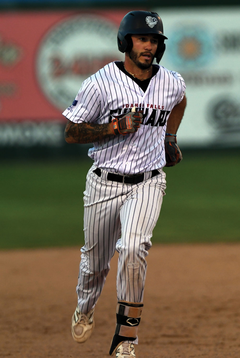 A baseball player in a pinstriped uniform and helmet running across the field, showcasing tattoos on his arm.