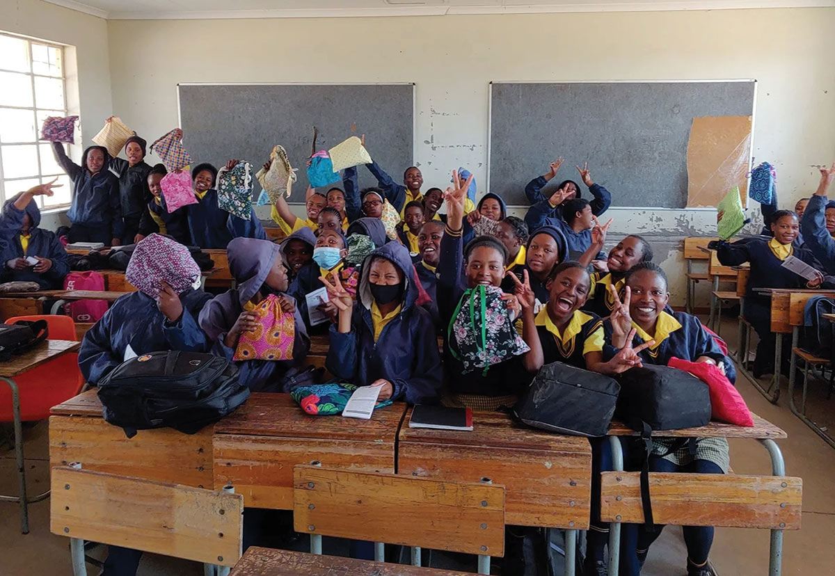A classroom of smiling students enthusiastically holding up colorful drawstring bags