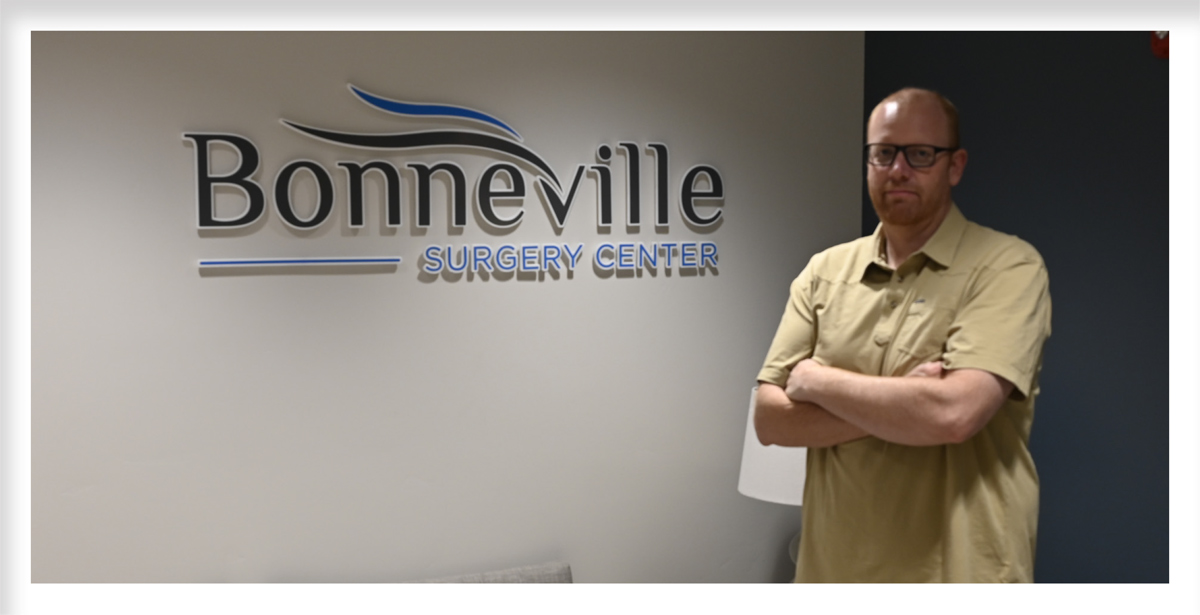 Administrator Adam Shurtz stands with arms crossed in front of a wall featuring the Bonneville Surgery Center logo sign.