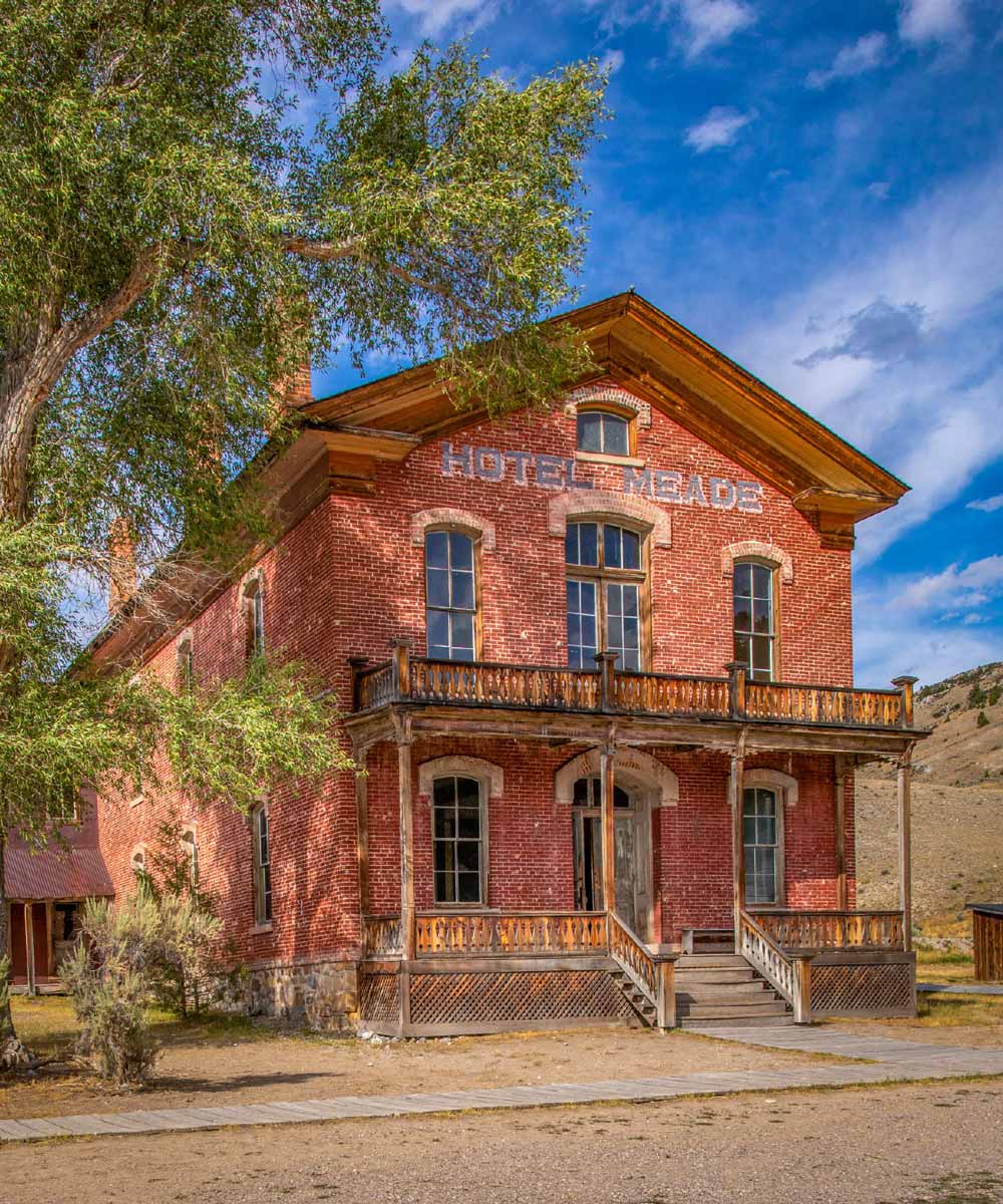 A two-story historic red brick building with wooden balconies, labeled "Hotel Meade," under a blue sky with soft white clouds.
