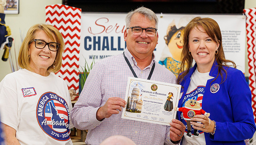 Three people smiling while holding a recognition certificate and a small plush toy.