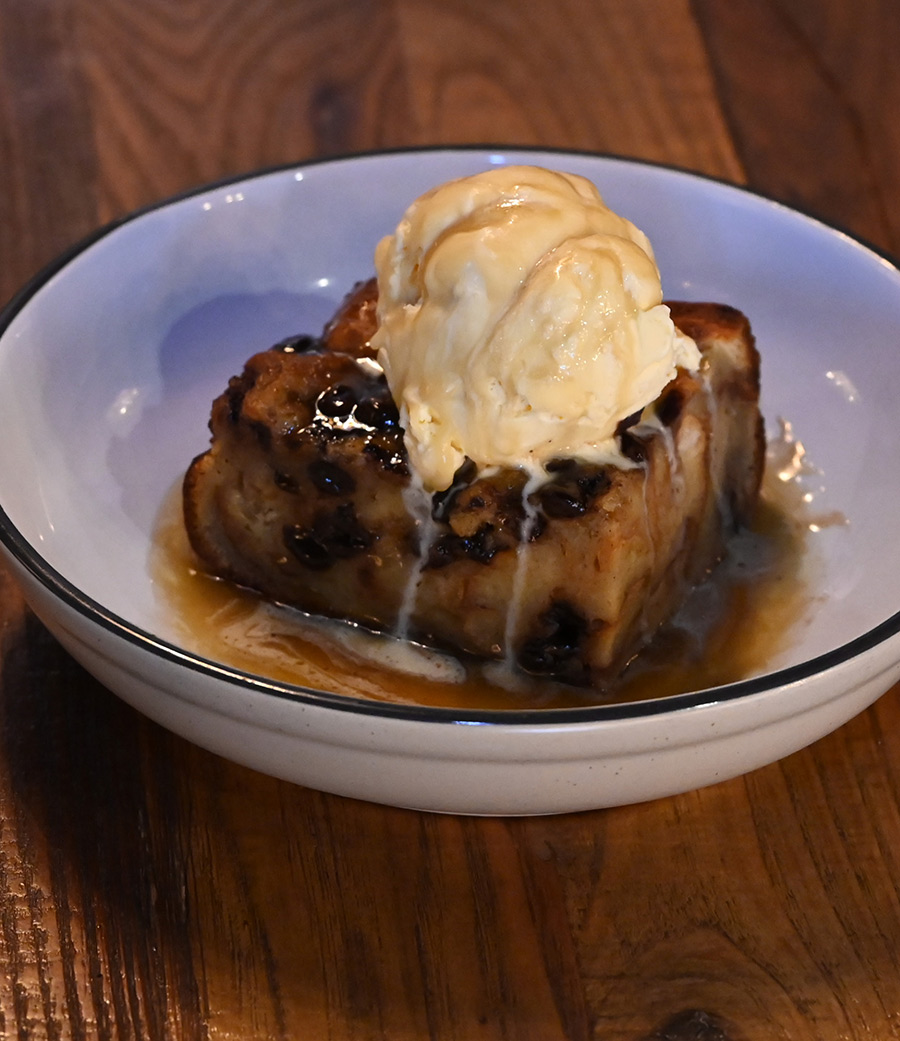 A dish of chocolate chip bread pudding topped with melting vanilla ice cream and caramel sauce.
