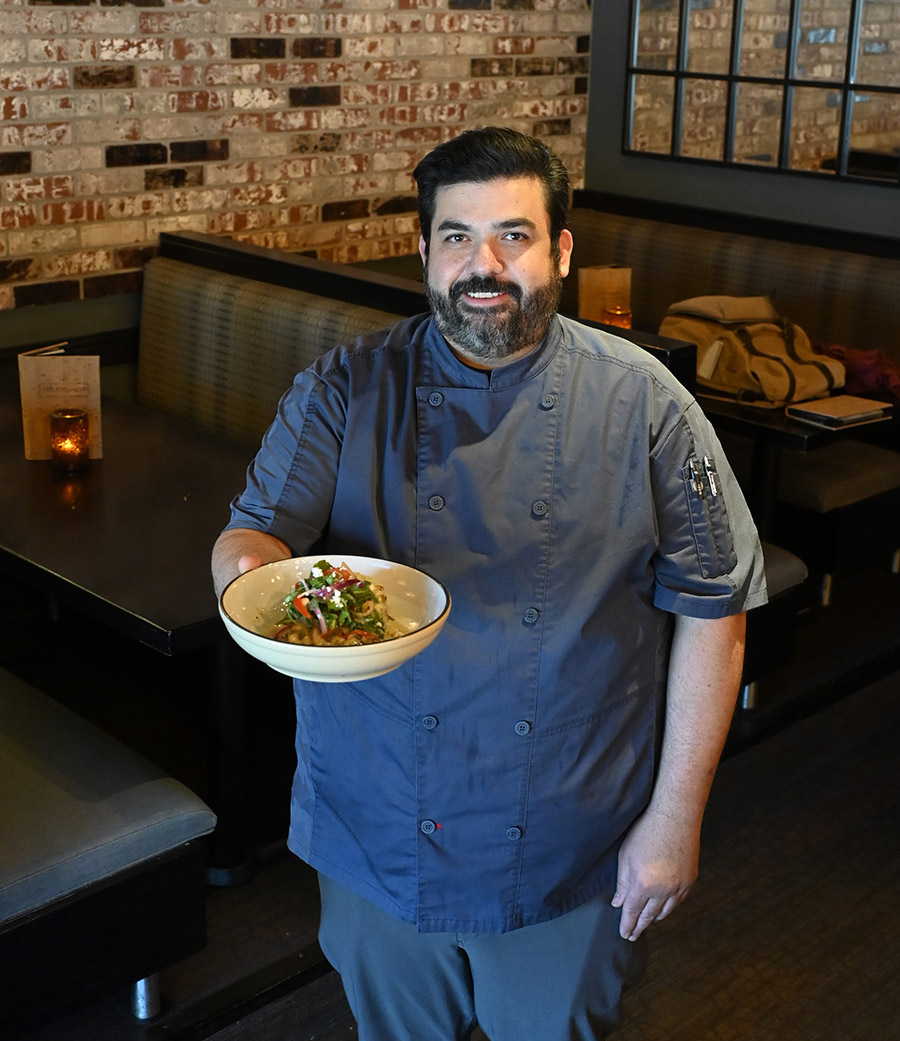 Chef Aaron McGregor stands inside the restaurant holding a freshly prepared gourmet culinary dish.