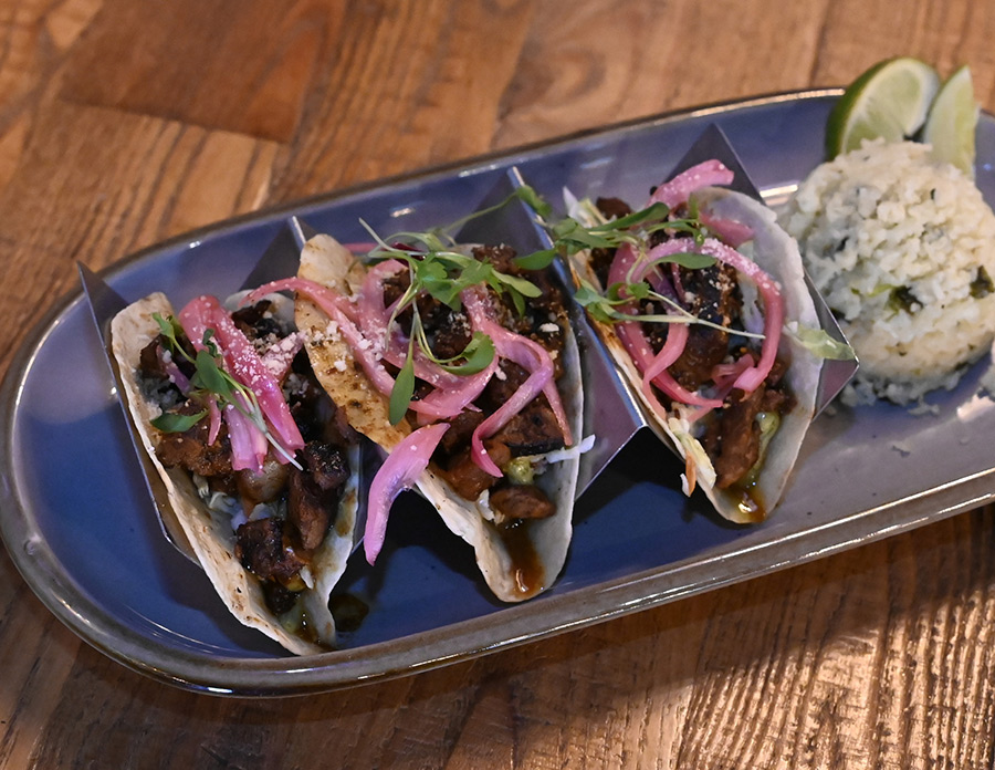 Three carne asada tacos topped with pickled onions, served with a side of rice.