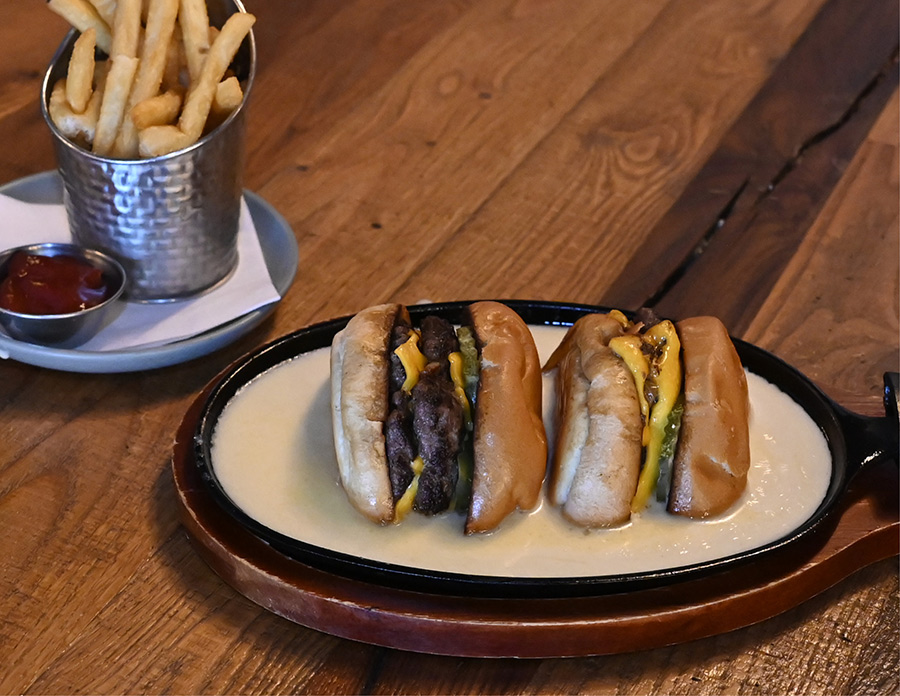 Two juicy smash burgers served in a skillet of melted cheese sauce alongside French fries.