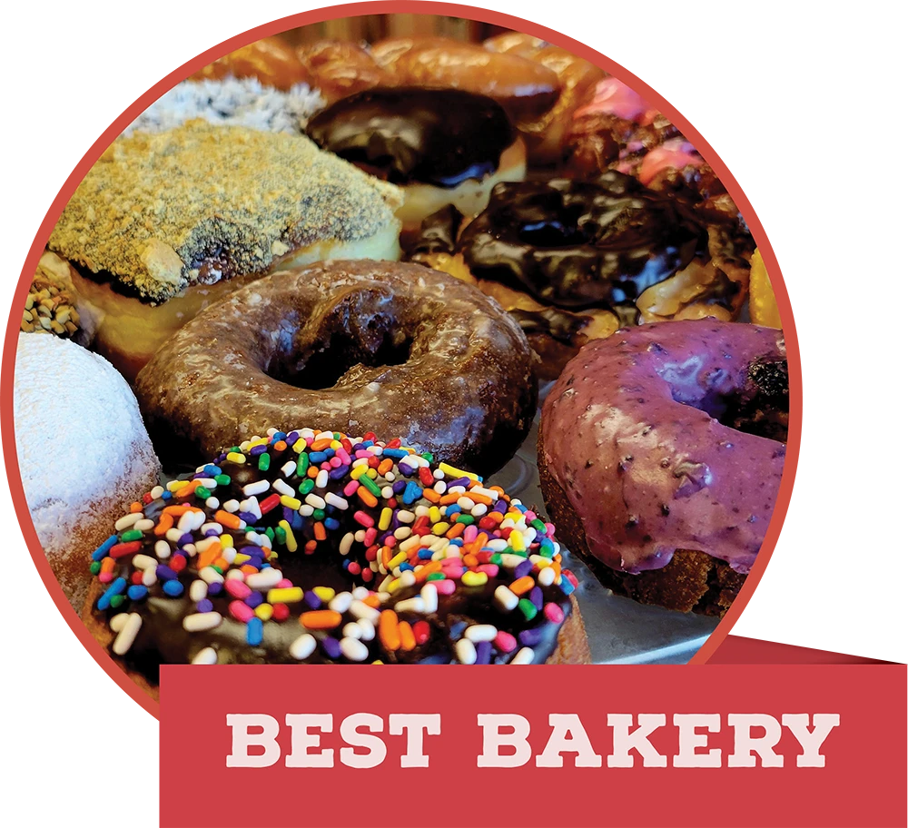 A colorful assortment of frosted, powdered, and sprinkled donuts, featuring a red banner that reads "BEST BAKERY."