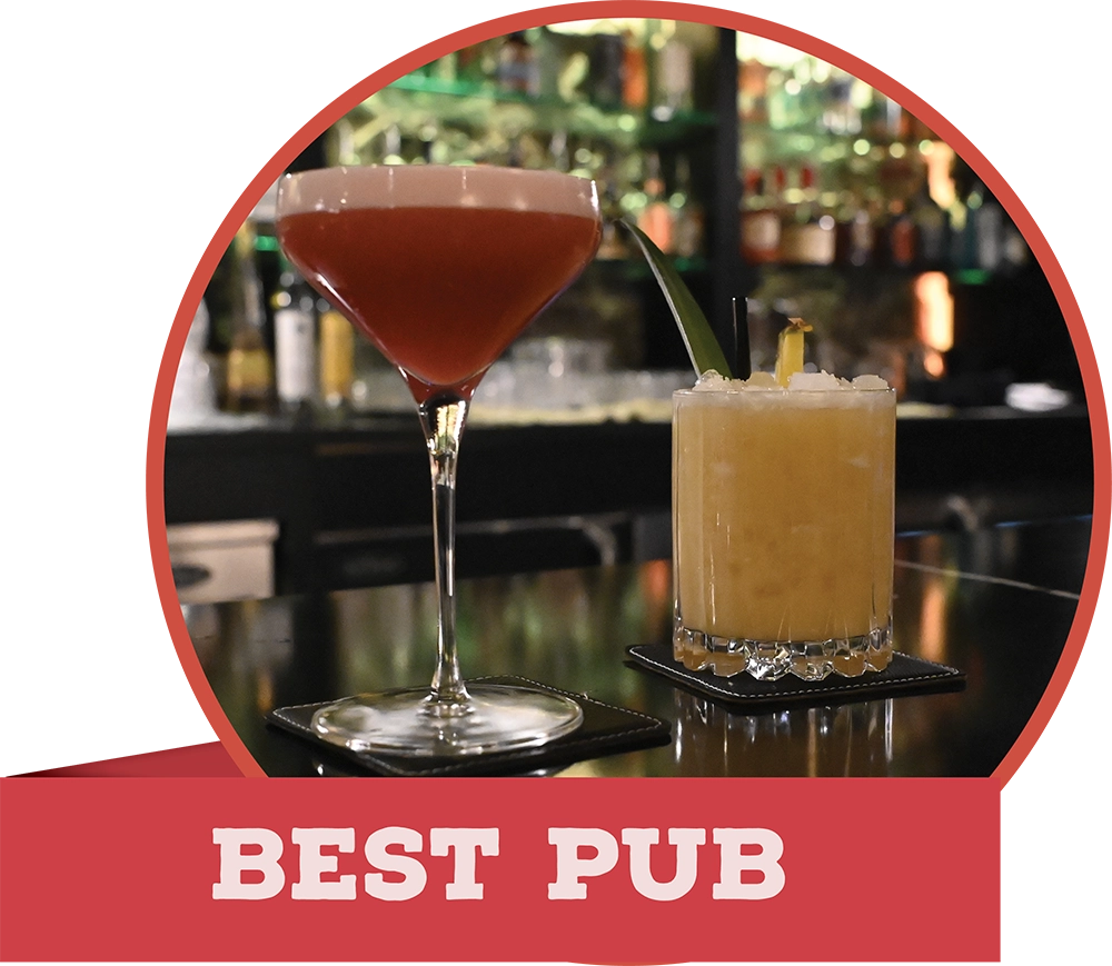 Two vibrant cocktails on a dark bar counter with a blurred bottle display behind them, labeled "BEST PUB" on a banner.