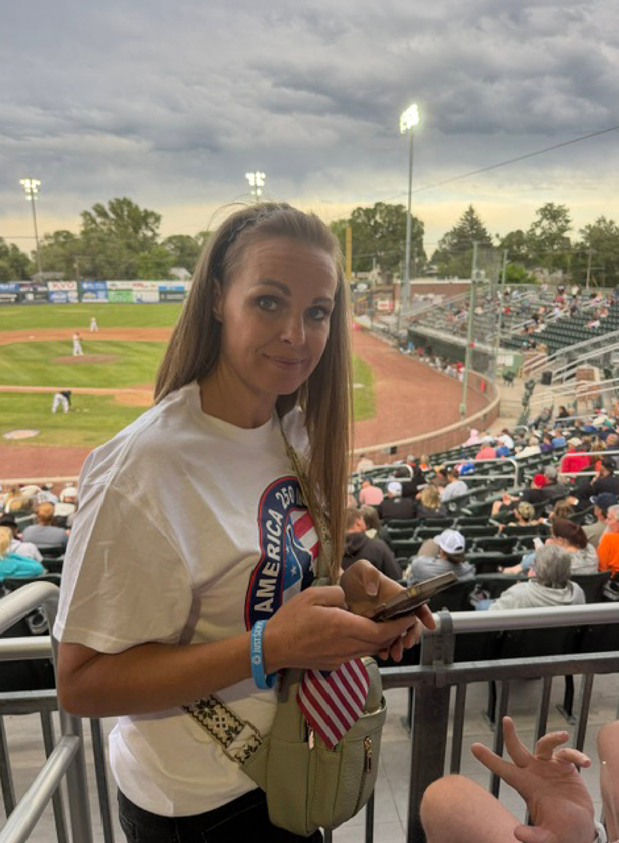 A woman holds a phone while standing in the grandstands at a baseball stadium.