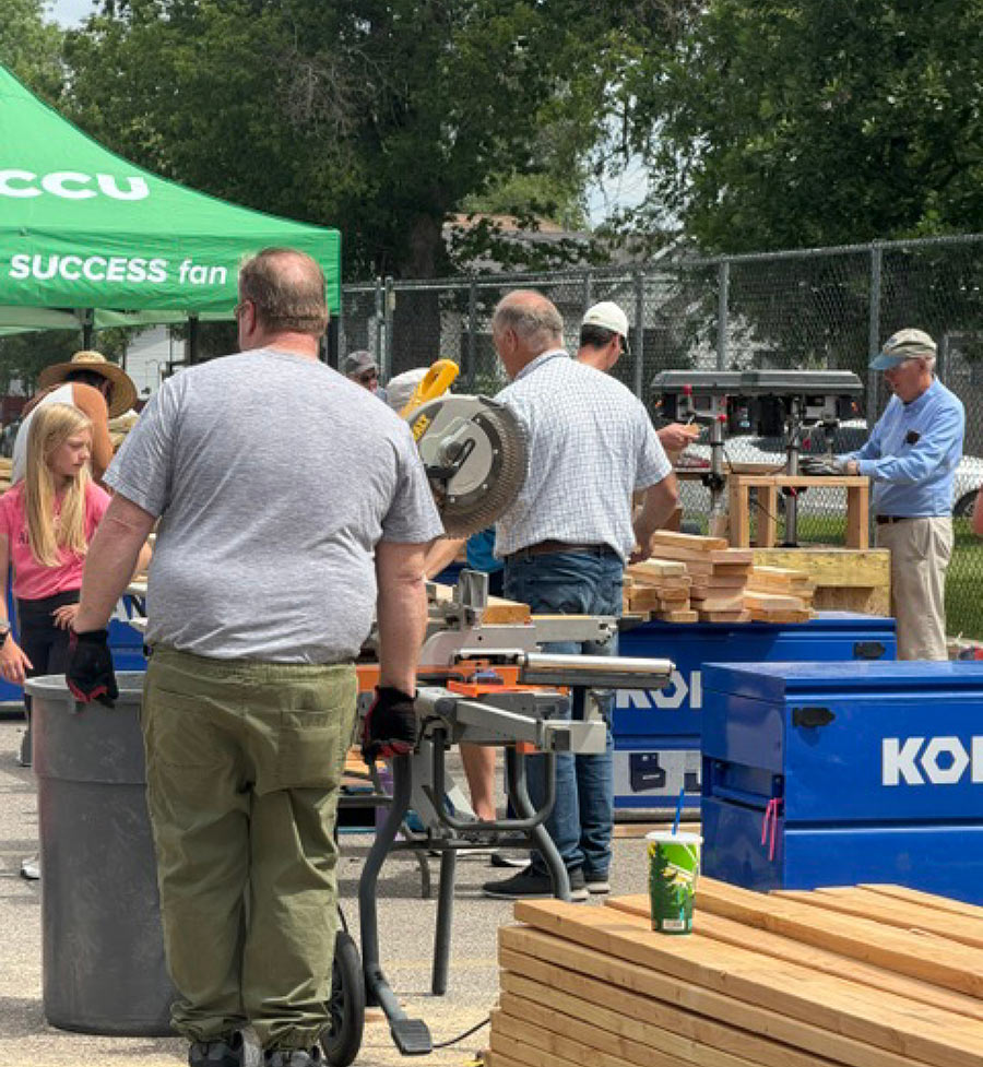 Volunteers use power tools and lumber to build wooden bed frames outdoors.