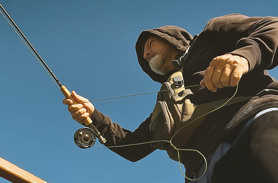 A low-angle view of a person wearing a hoodie while fly fishing.