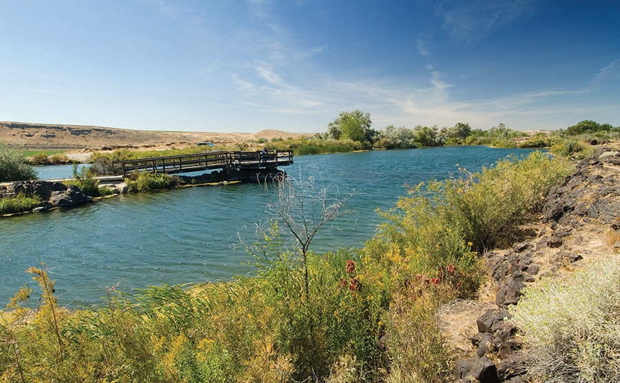 A wooden fishing pier extends over a wide river under a clear sky.