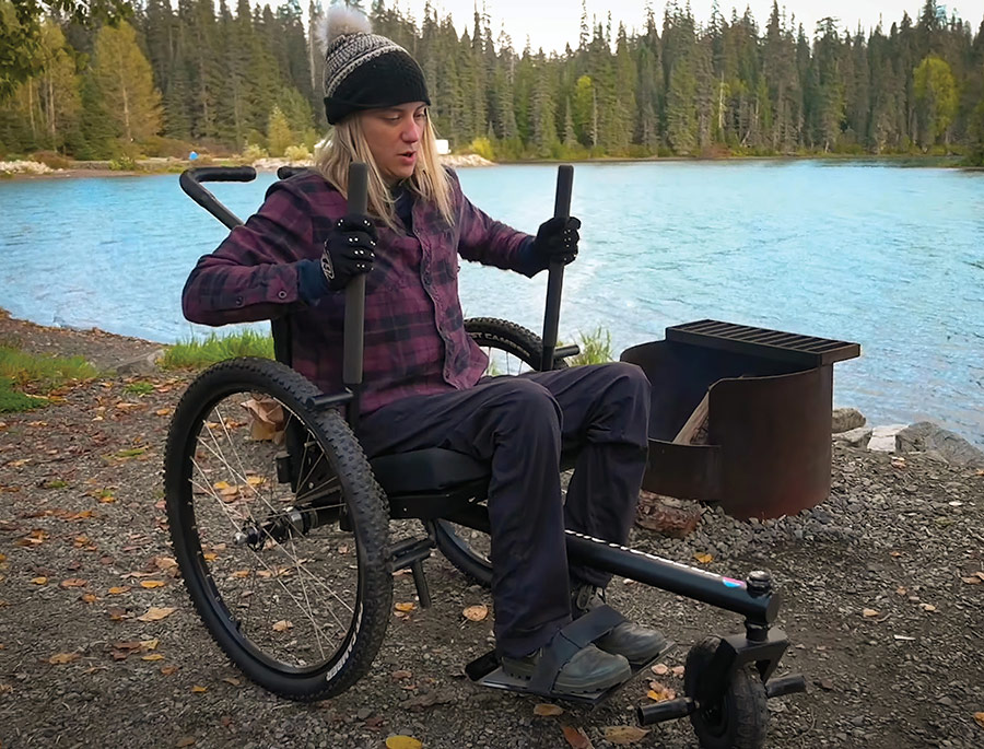 A person sitting in an all-terrain wheelchair near a bright blue lake.