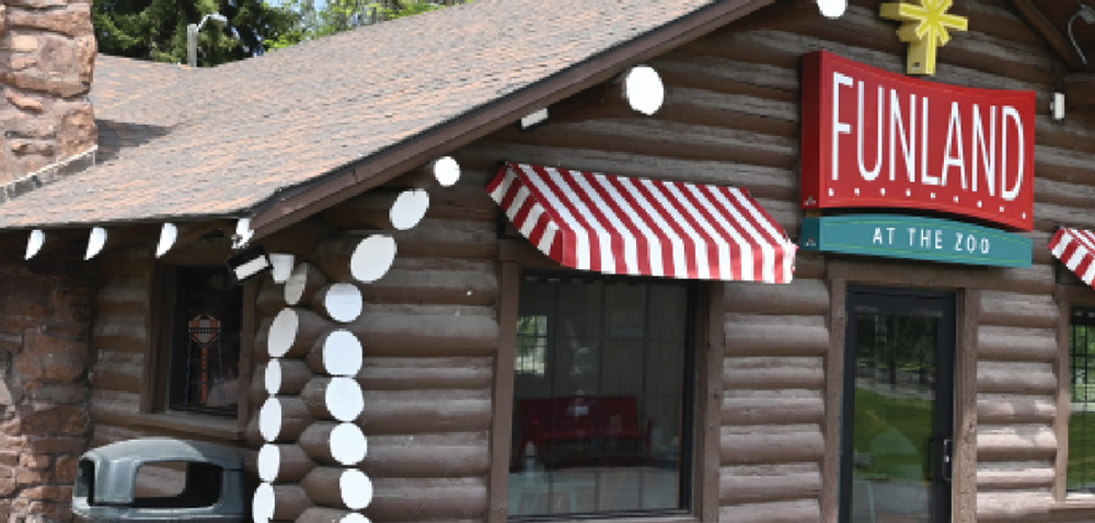 Exterior of a log cabin style building with striped awnings and a red sign reading Funland at the Zoo.