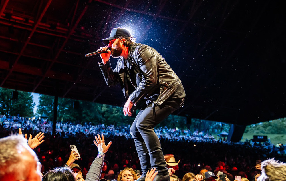Nate Smith performing live on stage, leaning forward toward cheering fans with hands raised.