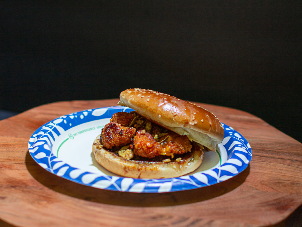 Crispy fried chicken sandwich on a sesame seed bun served on a blue pattern paper plate.