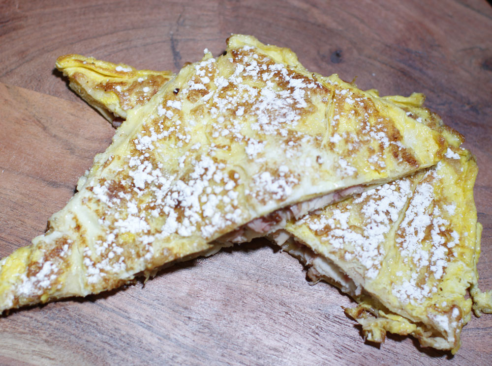 Two folded crepe-style sandwiches dusted with powdered sugar on a wooden board.