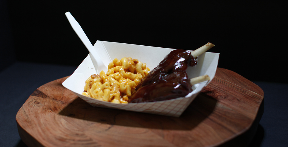 Barbecue ribs on the bone served with creamy mac and cheese in a paper food basket.