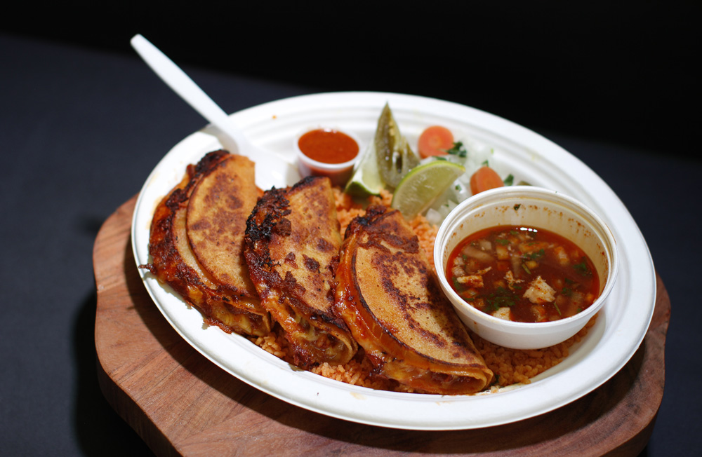 Birria tacos served on orange rice with a cup of consommé broth and lime wedges.