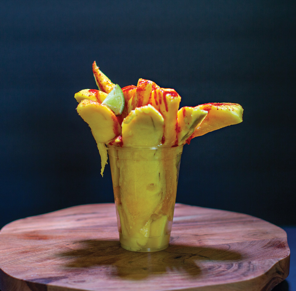 Fresh mango spears served in a cup, drizzled with chamoy sauce, chili seasoning, and a lime wedge.