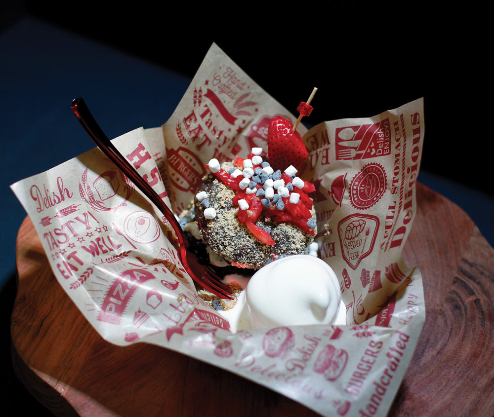 Chocolate s'mores dessert with mini marshmallows, graham cracker crumbles, a fresh strawberry, and vanilla ice cream.