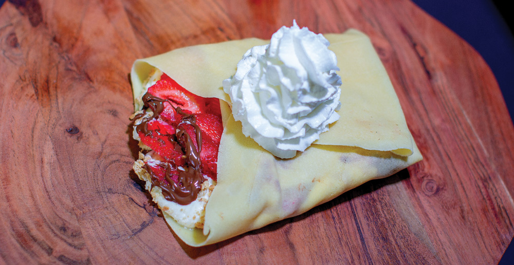Folded crepe filled with sliced strawberries, chocolate drizzle, and topped with a swirl of whipped cream.
